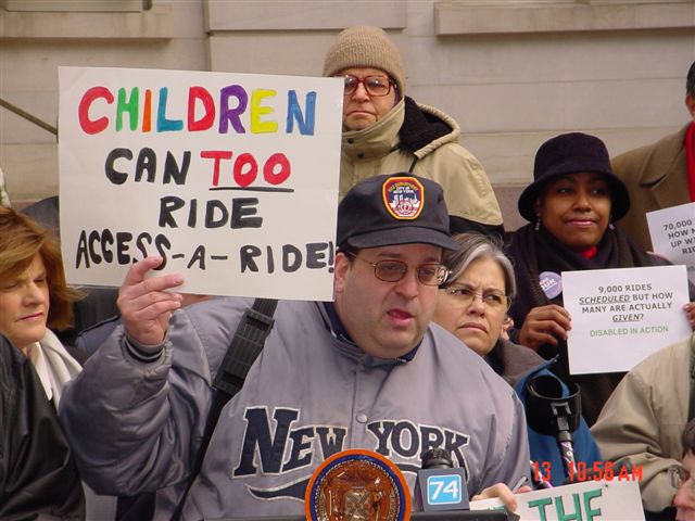 Photo of man holding sign stating Children Can Too Ride Access-A-Ride